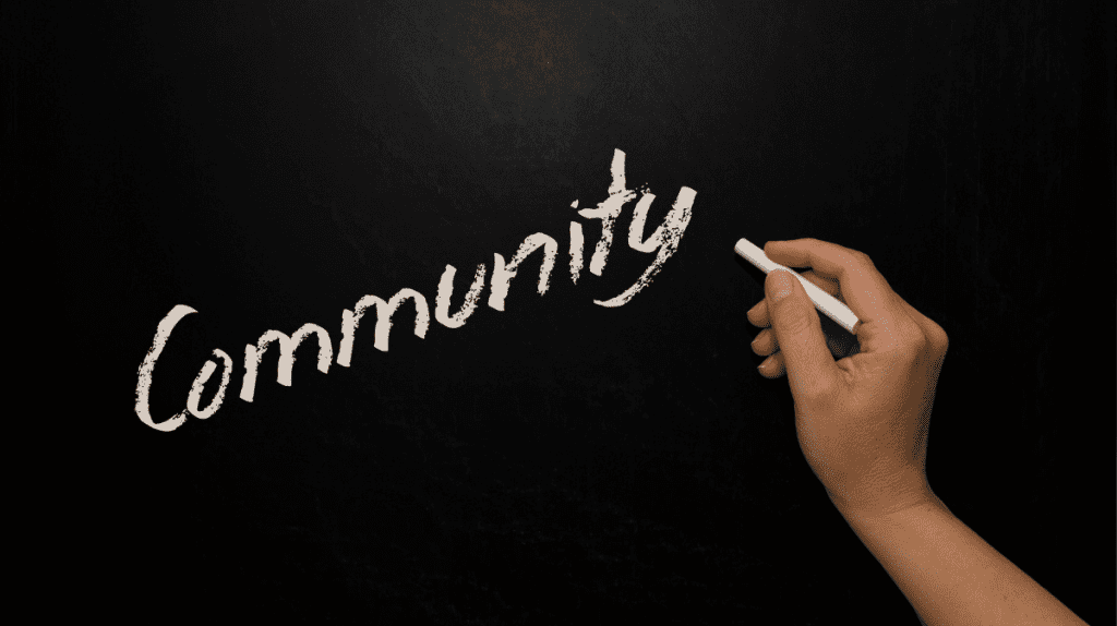 person writing the word community on a chalk board
